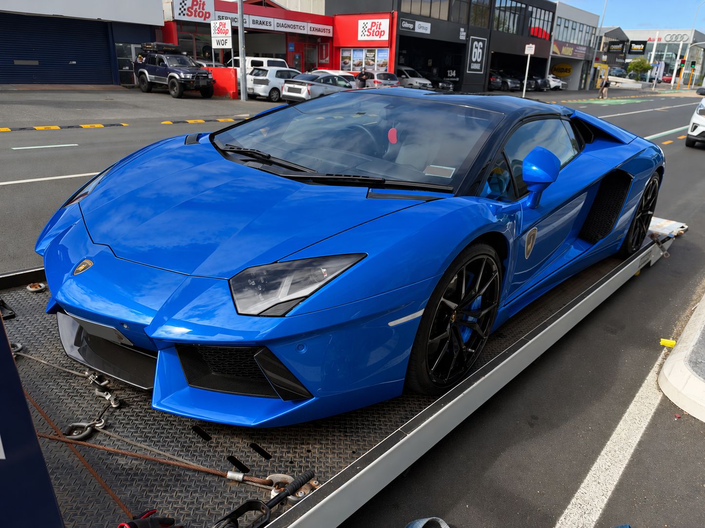 Front three-quarter view of a Lamborghini on a flatbed, showing its low front bumper and side skirt; edited blue bodywork.