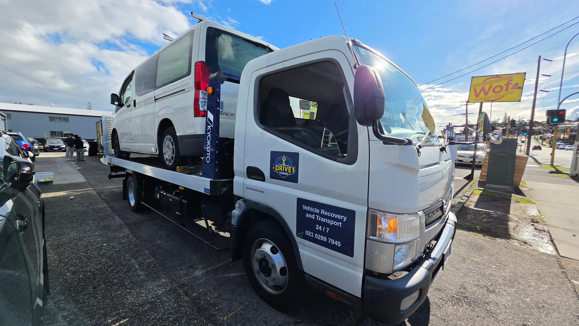Drive1 Towing flatbed transporting a Toyota Hiace under a bright Auckland sky.