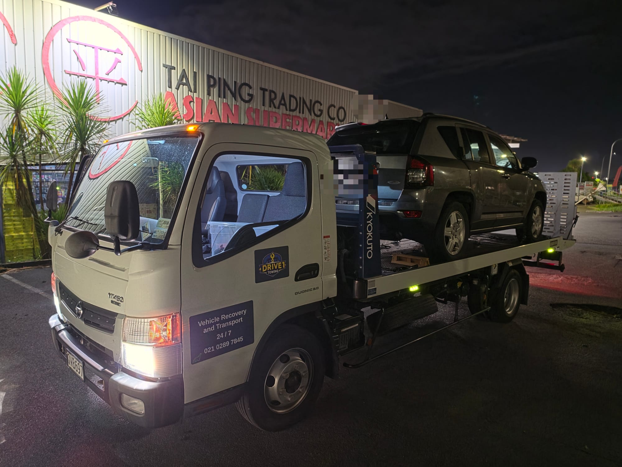Red sedan secured on Drive1 Towing flatbed at night in Auckland.